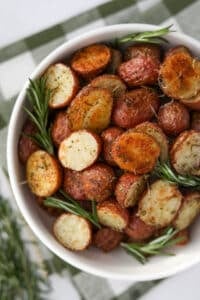 A bowl of roasted potatoes garnished with sprigs of fresh rosemary.