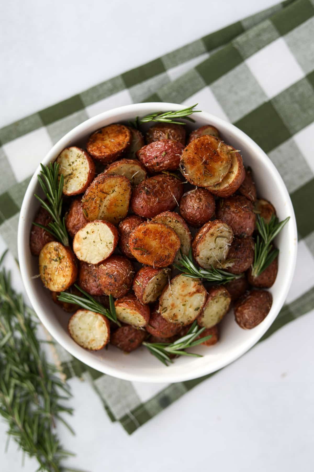 A bowl of roasted potatoes garnished with fresh rosemary sprigs.
