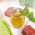 A small glass jar of homemade vinaigrette with a small spoon inside.