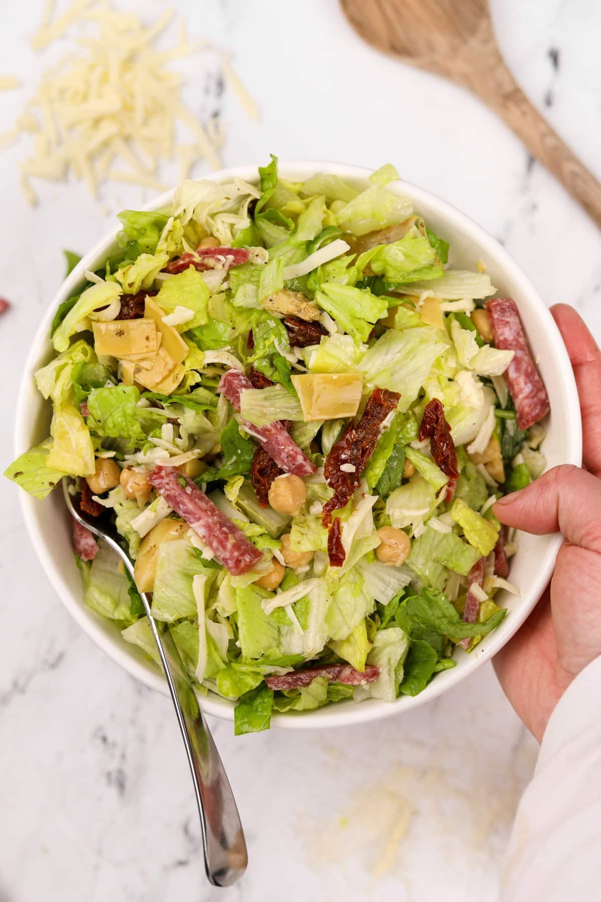 Holding a bowl of chopped salad, featuring chopped salami and mozzarella.