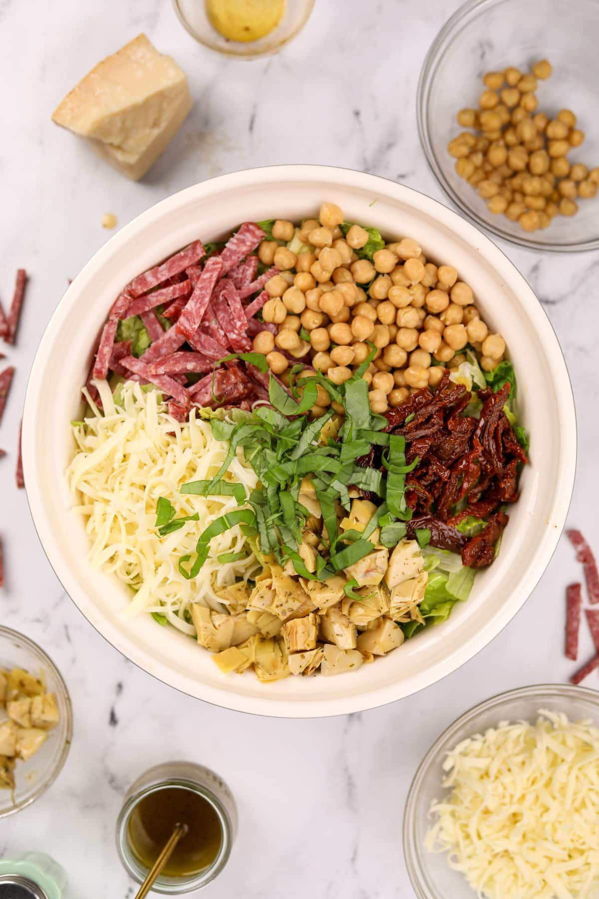A large salad bowl filled with salad, including sections of toppings: mozzarella, artichokes, basil, sun dried tomatoes, chickpeas, and salami.