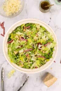 A bowl of chopped salad featuring chopped salami pieces.