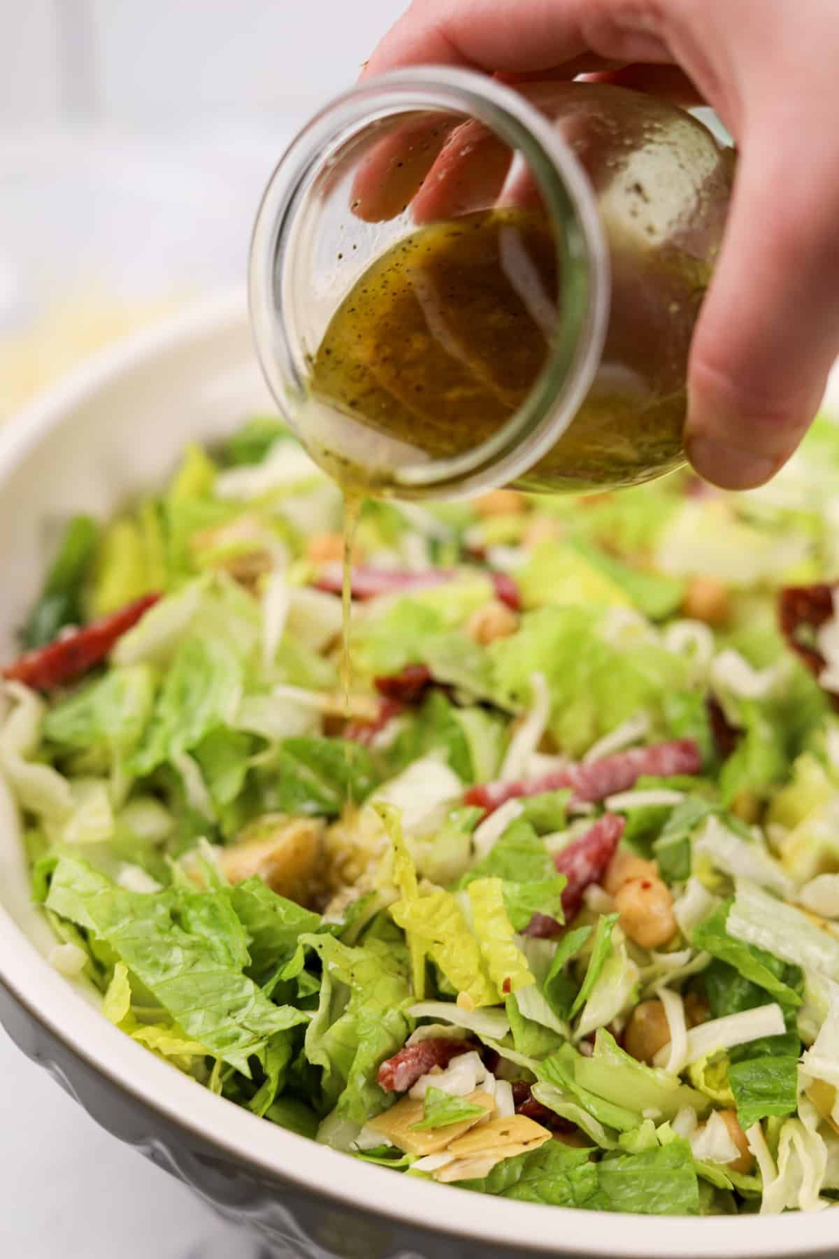 Pouring salad dressing over a chopped salad.