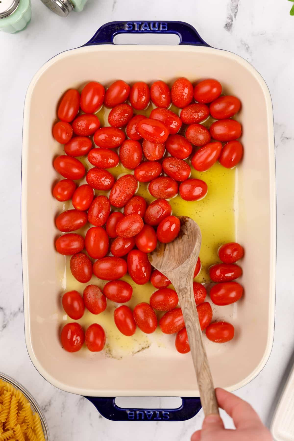 Stirring olive oil and grape tomatoes together in a baking dish.