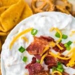 A creamy dip in a bowl, garnished with bacon, cheese, and green onion.
