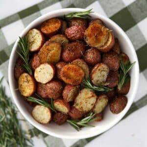 A white bowl filled with roasted baby potatoes, garnished with several sprigs of fresh rosemary.