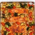 Salmon fillets spaced on a baking sheet, surrounded by cooked vegetables.