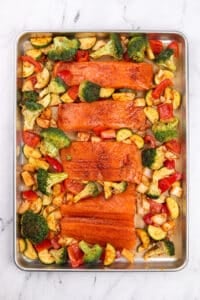A sheet pan with seasoned salmon fillets and various vegetables.