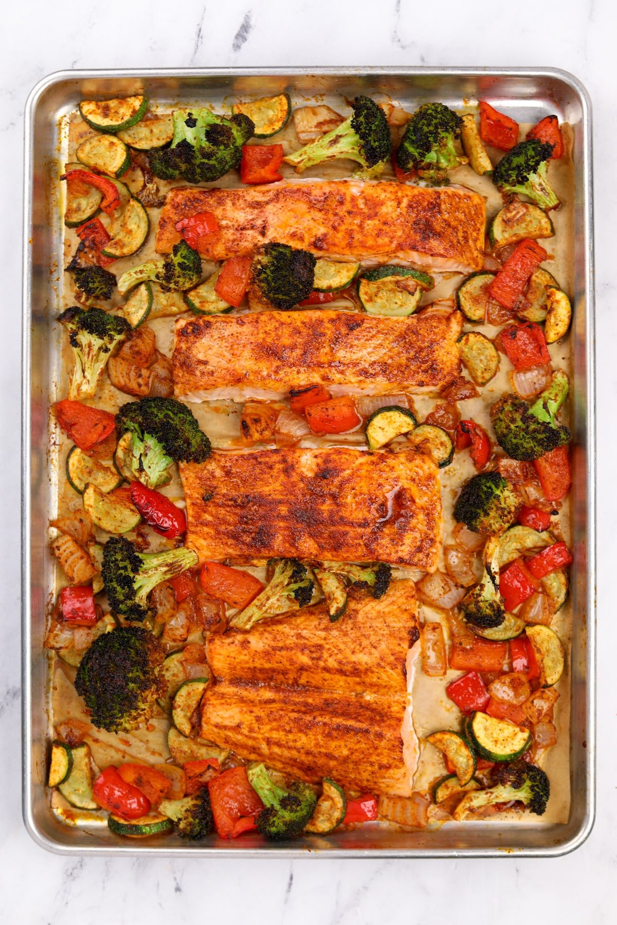 A sheet pan with roasted vegetables and salmon fillets.
