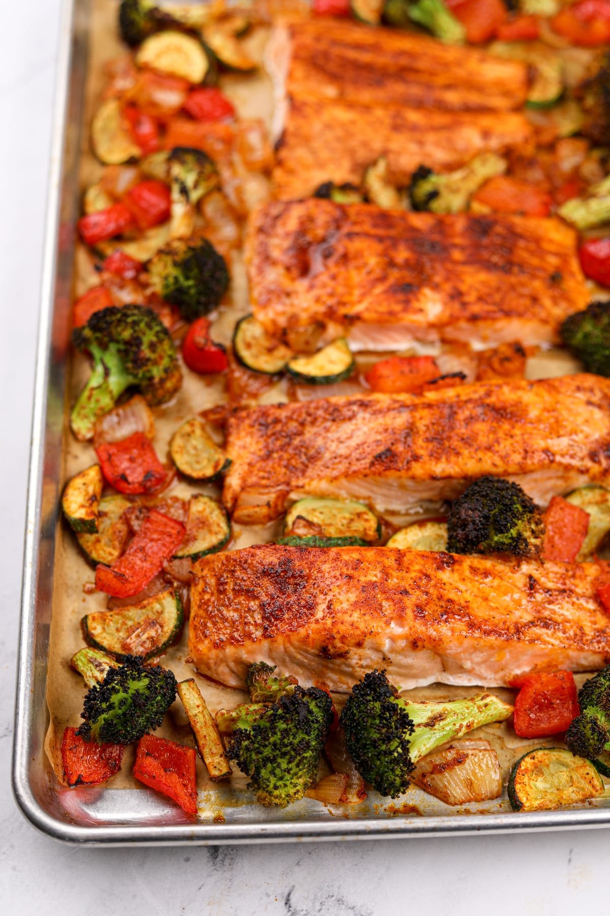 A sheet pan filled with roasted vegetables and salmon fillets.