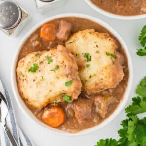 A white bowl filled with beef stew and topped with homemade dumplings.