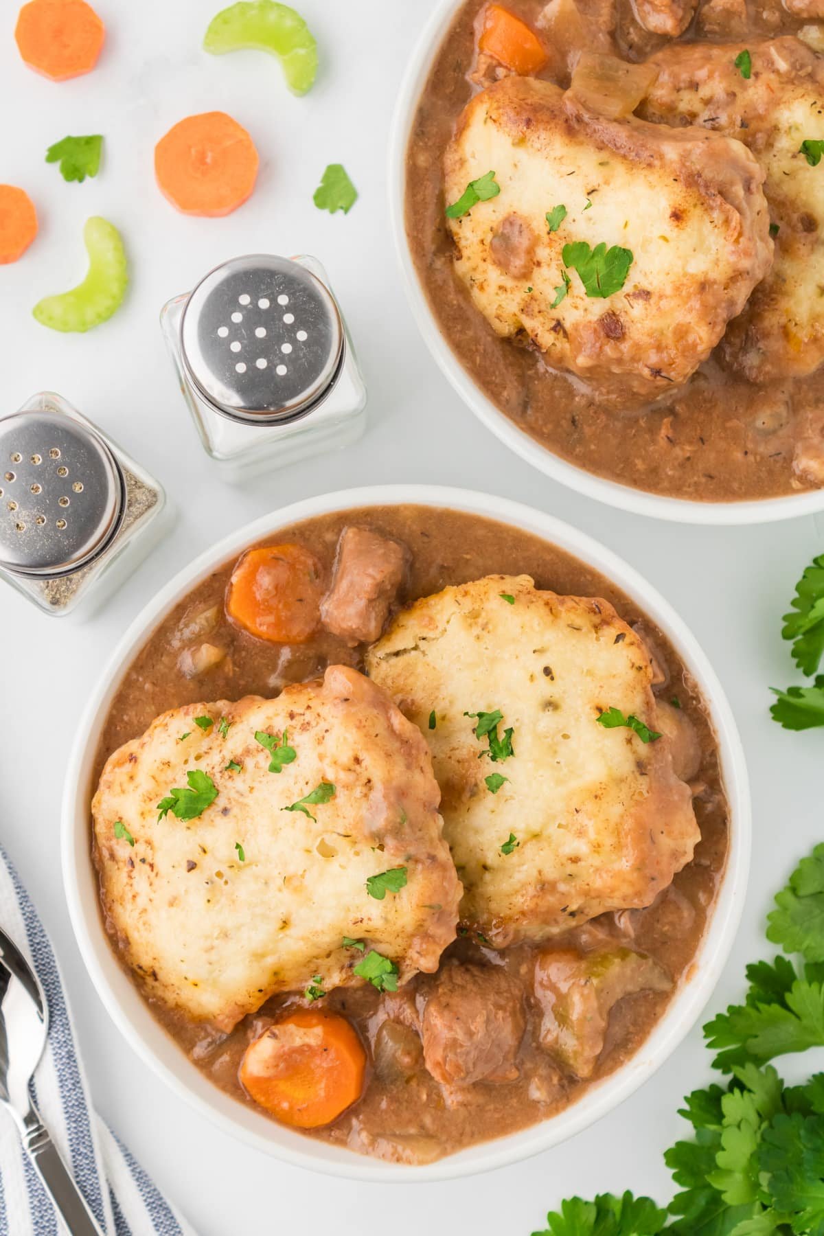 A bowl of beef stew topped with two dumplings, garnished with parsley.