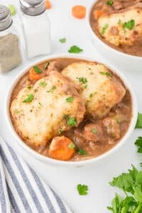 A bowl filled with beef stew and topped with two homemade dumplings.