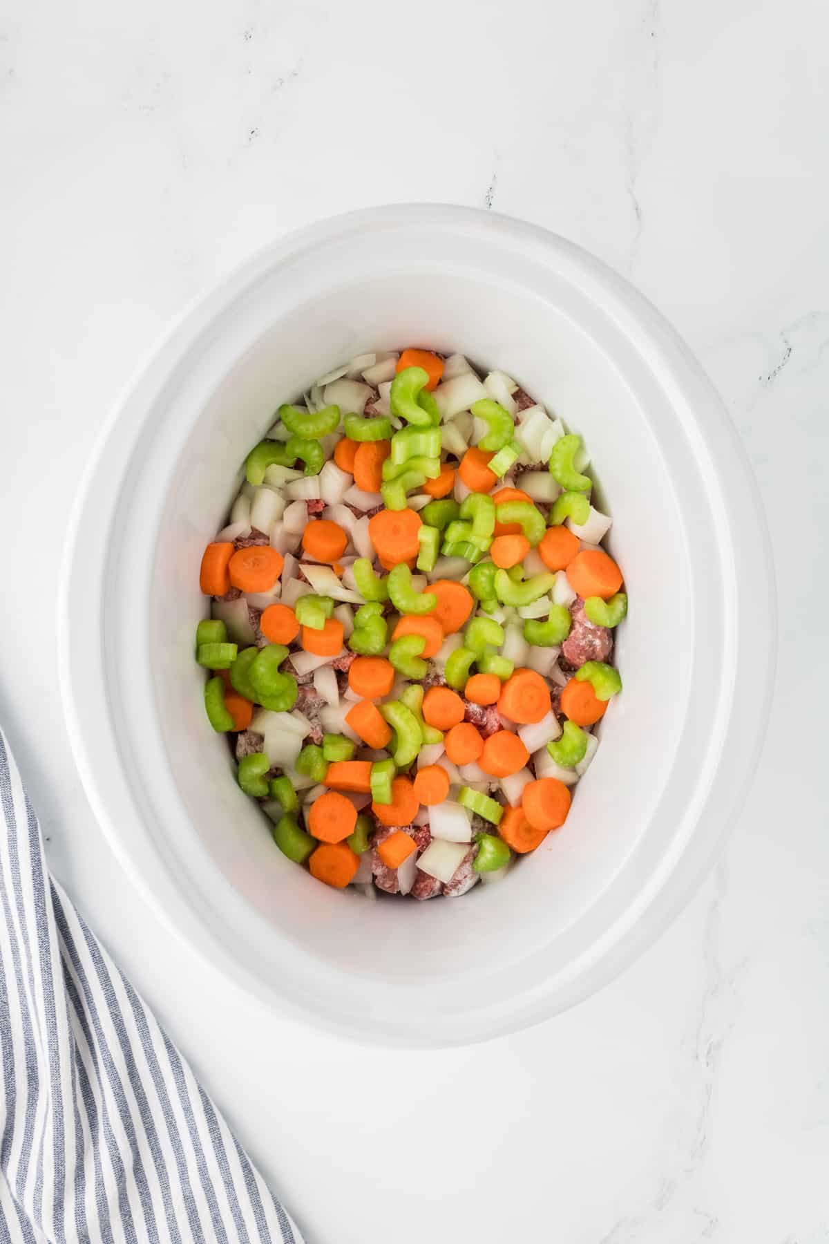 A slow cooker with beef cubes, celery, carrots, and onions layered inside.