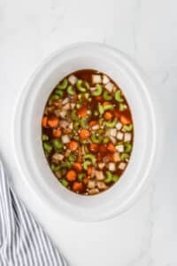 A slow cooker with vegetables and beef broth.