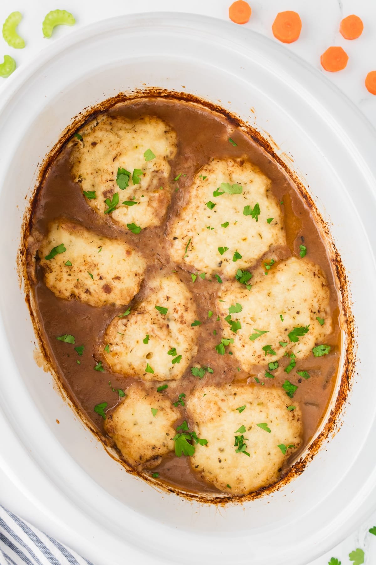 A white slow cooker insert filled with beef stew topped with homemade dumplings.