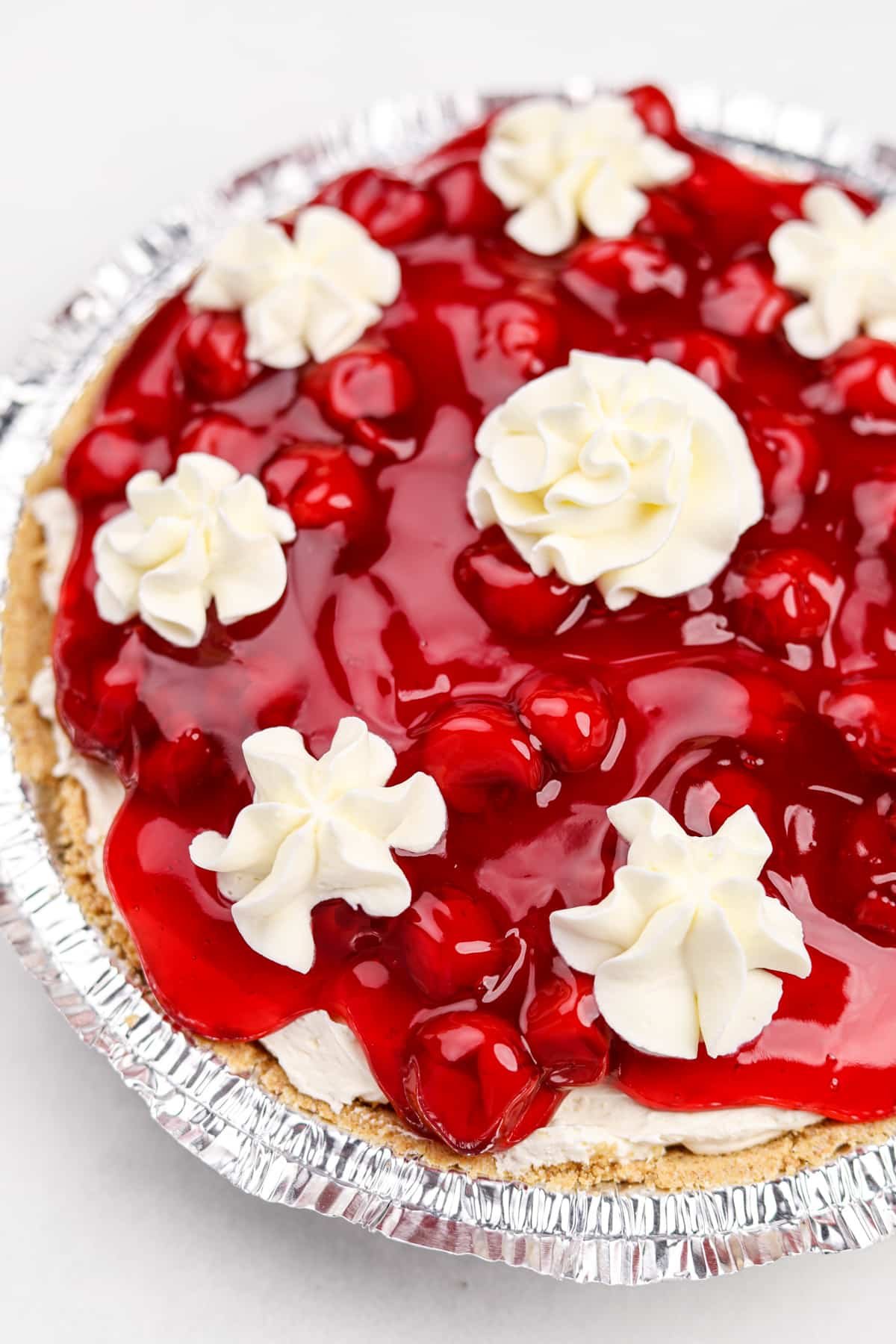 A cherry cheesecake topped with dollops of whipped cream.