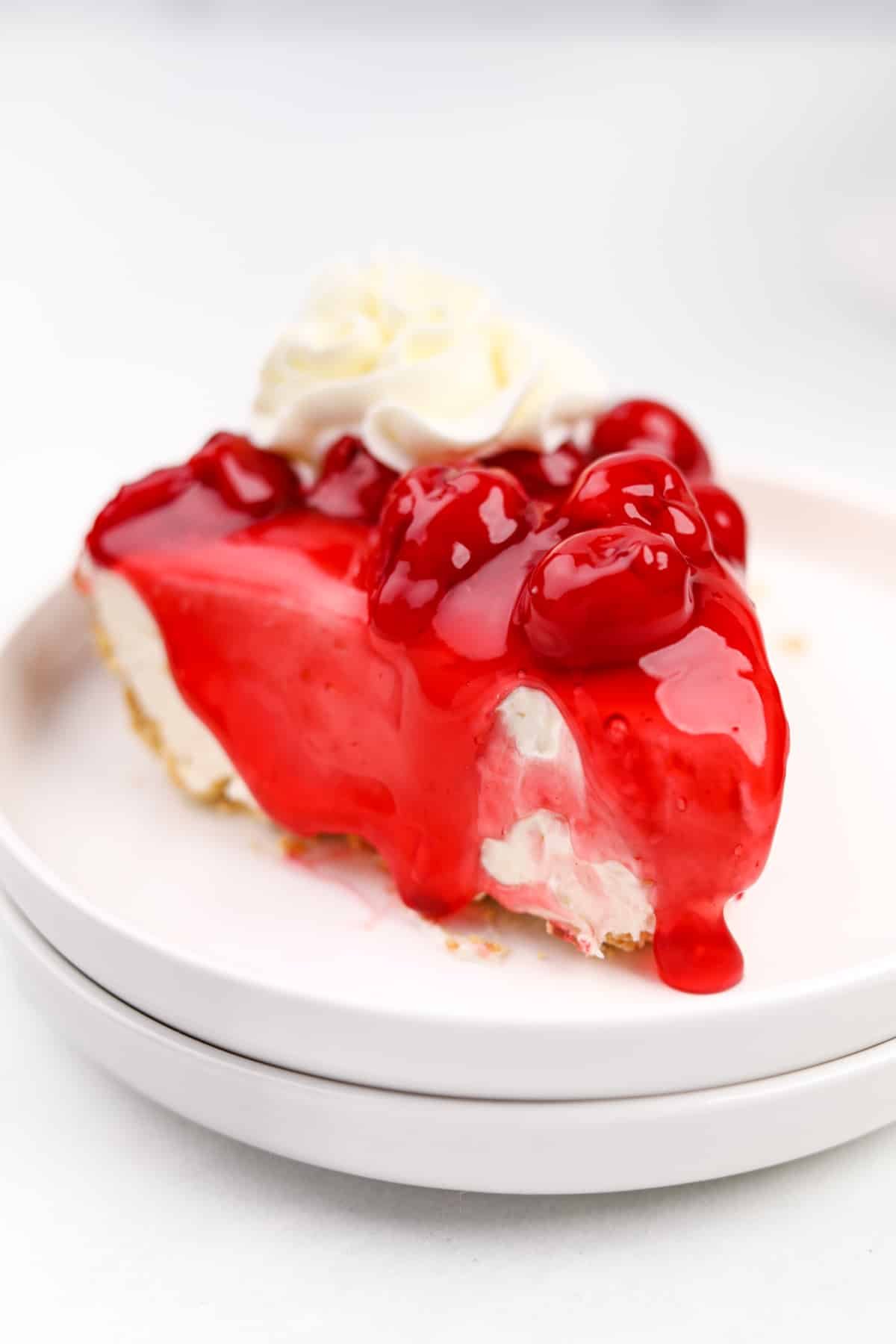 A slice of cheesecake topped with cherry topping and whipped cream.