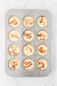 A muffin pan that has each cup filled with an egg mixture and topped with crumbled bacon.