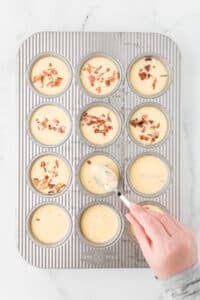 Pressing bacon down under an egg-based batter in a muffin pan.