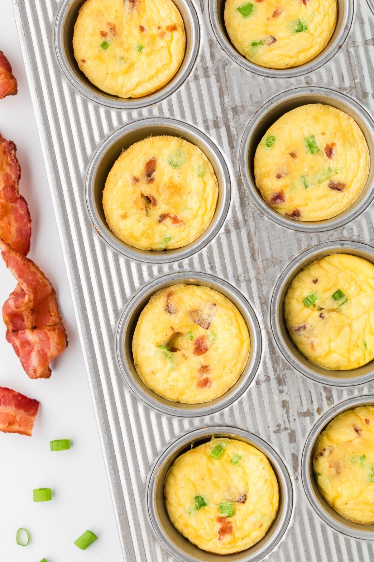 A muffin pan filled with egg bites and topped with bacon.