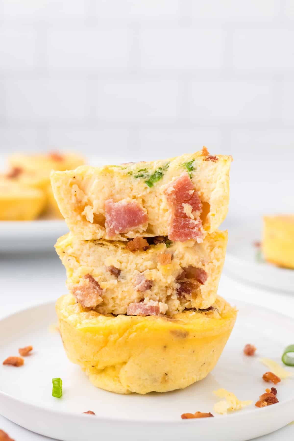A stack of three egg cups filled with bacon and garnished with green onion.