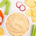 A bowl of onion dip surrounded by fresh veggies and chips.