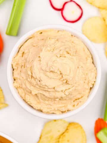 A bowl of onion dip, with vegetables and potatoes garnished around.