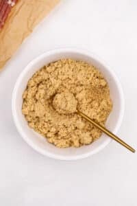 A small bowl of brown sugar being mixed with a small gold spoon.