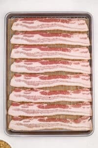 Raw bacon strips in an even layer on a wire rack set inside of a baking pan.