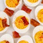 8 deviled egg halves topped with a square of bacon.