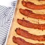 Slices of cooked bacon on a parchment lined baking sheet. The text box reads: "meal prep oven baked bacon"