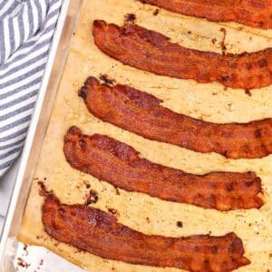 Slices of crispy bacon on a parchment lined baking sheet.