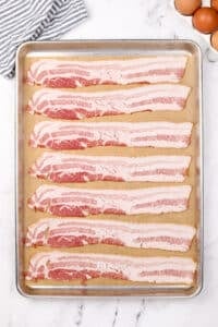 Eight slices of bacon on a parchment lined baking sheet.