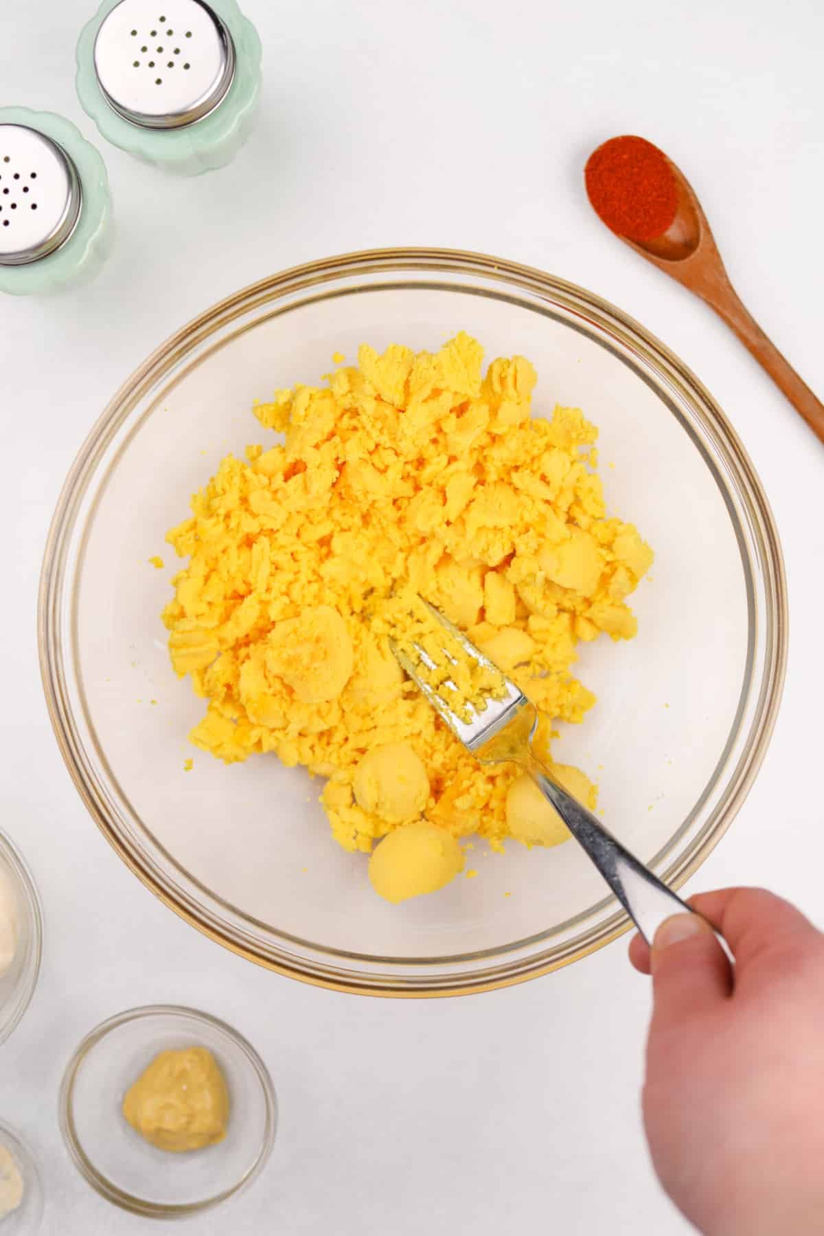 Mashing cooked egg yolks in a bowl with a fork.
