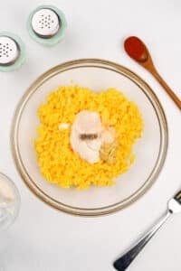 Adding mayonnaise and seasonings to a bowl of mashed egg yolk.