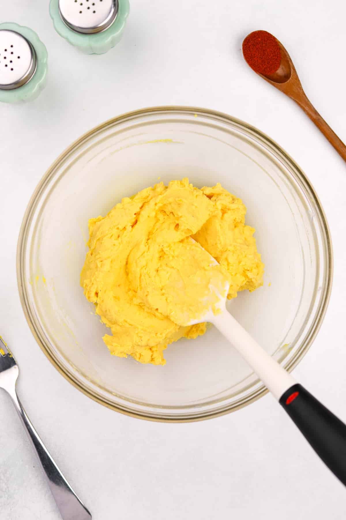Stirring together cooked egg yolks with mayonnaise in a bowl.