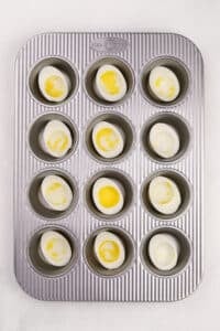 A muffin pan with cooked egg white halves in it.