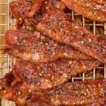 A baking rack stacked with candied bacon slices dotted with red pepper flakes.
