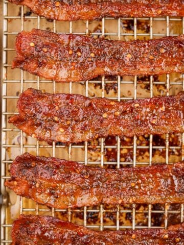 A wire cooking rack filled with cooked bacon that's been candied with brown sugar and crushed chilies.