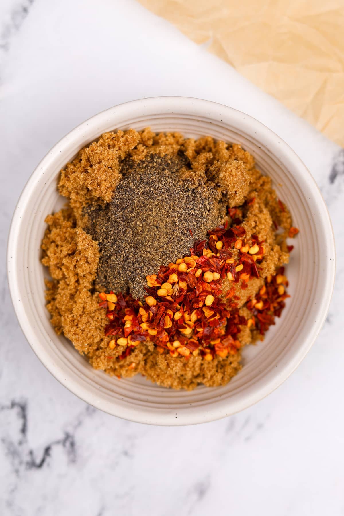 A small bowl with brown sugar, crushed chilies, and black pepper.