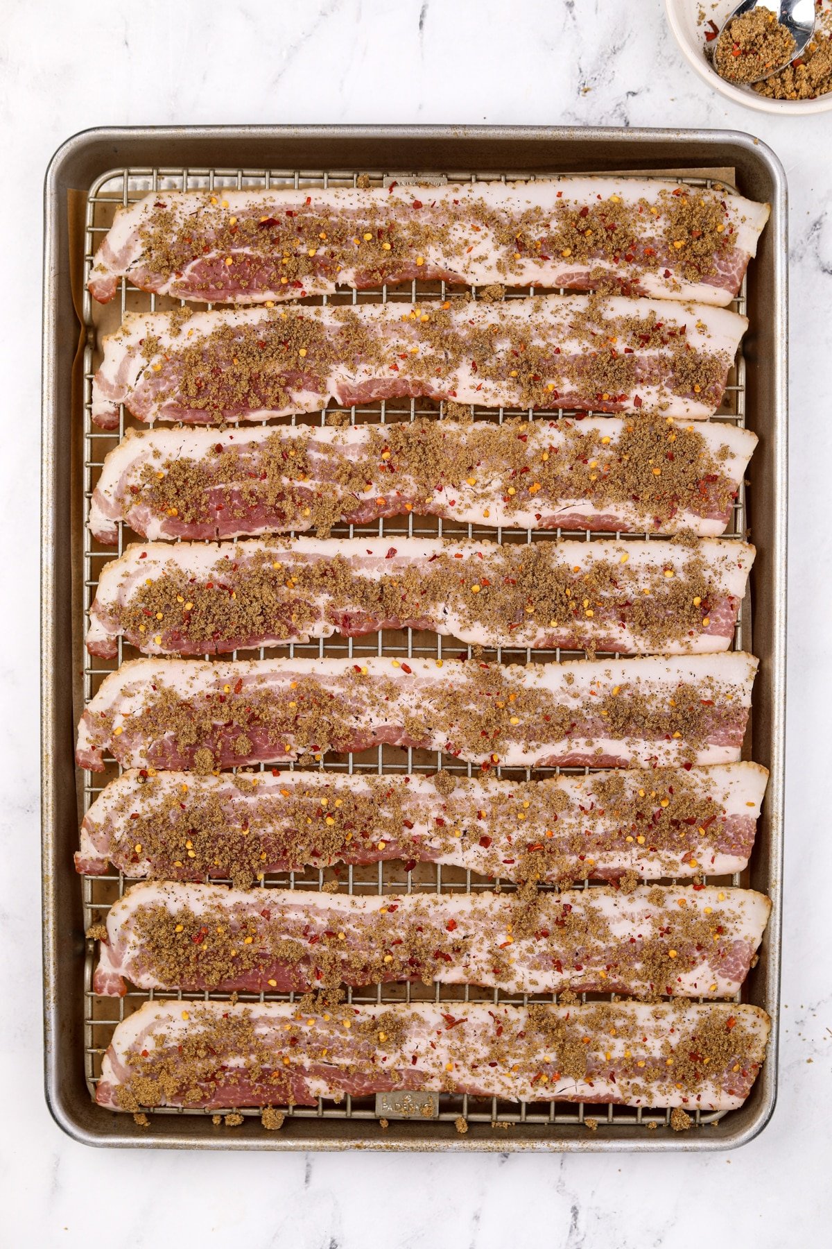 A baking sheet filled with bacon that has been sprinkled with brown sugar.