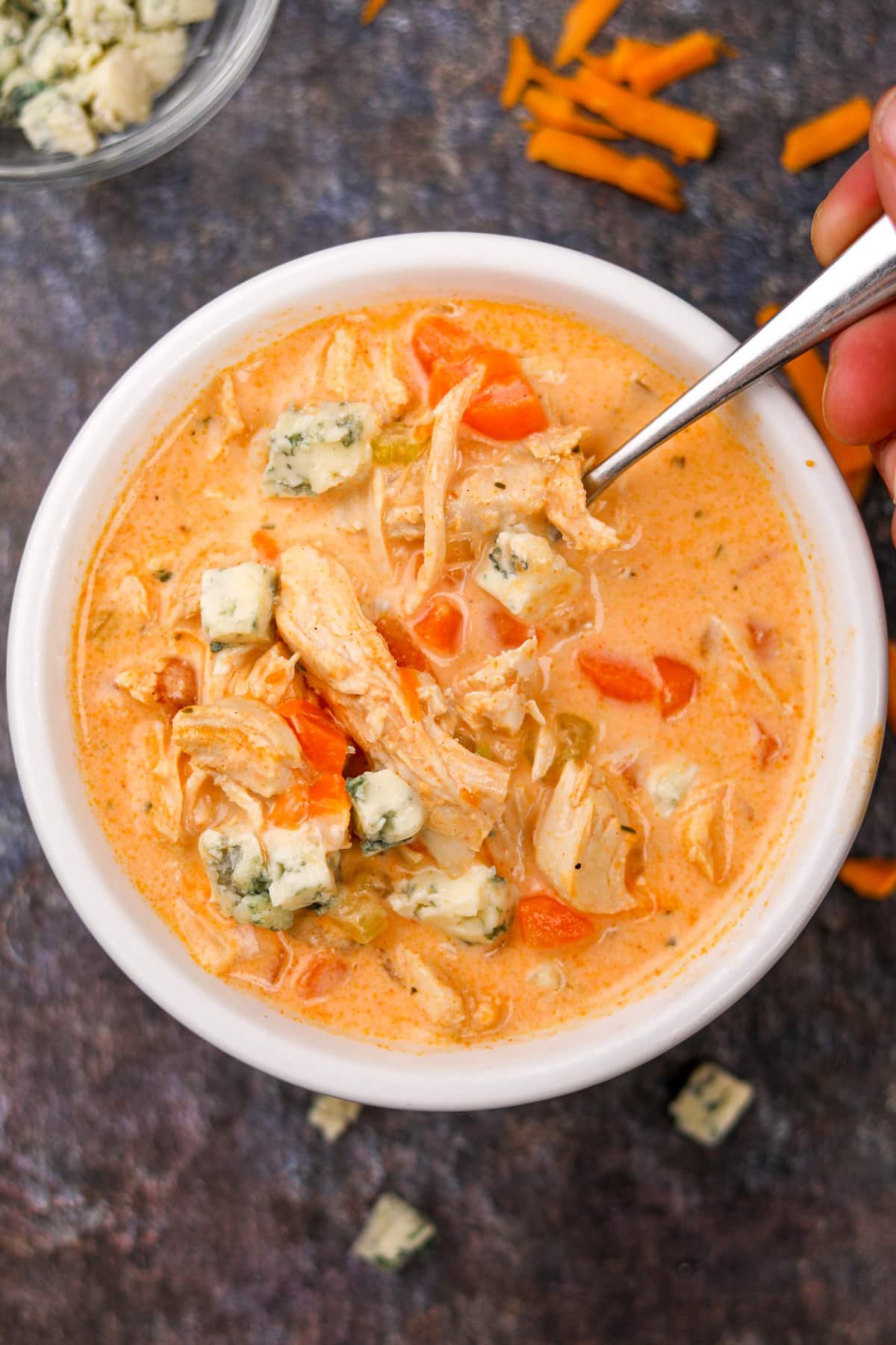 A bowl of spicy chicken soup with a spoon taking a portion.