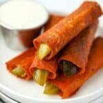 A stack of cheesy fried pickles with a small container of ranch dressing in the background.