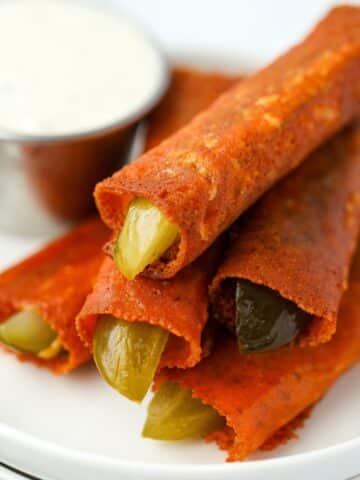 A stack of cheesy fried pickles with a small container of ranch dressing in the background.