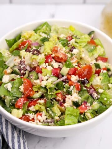 A white bowl filled with a leafy salad and Greek-inspired vegetables.