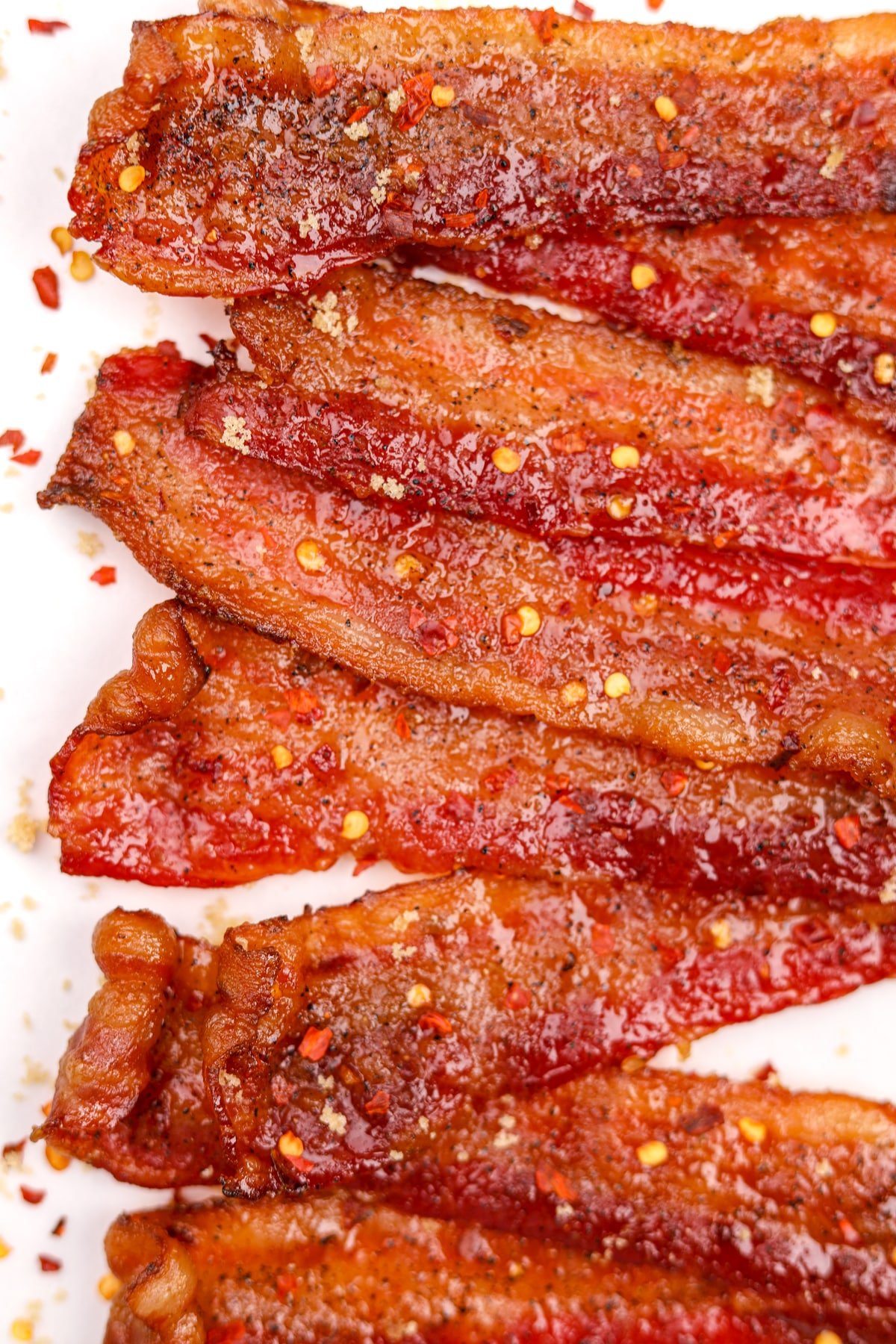 Slices of cooked bacon dotted with red pepper flakes.