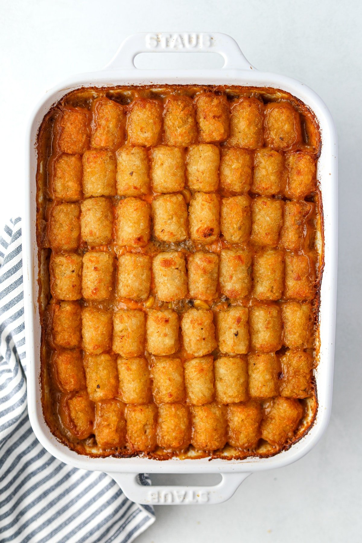 A white baking dish filled with ground beef and potato tot casserole.