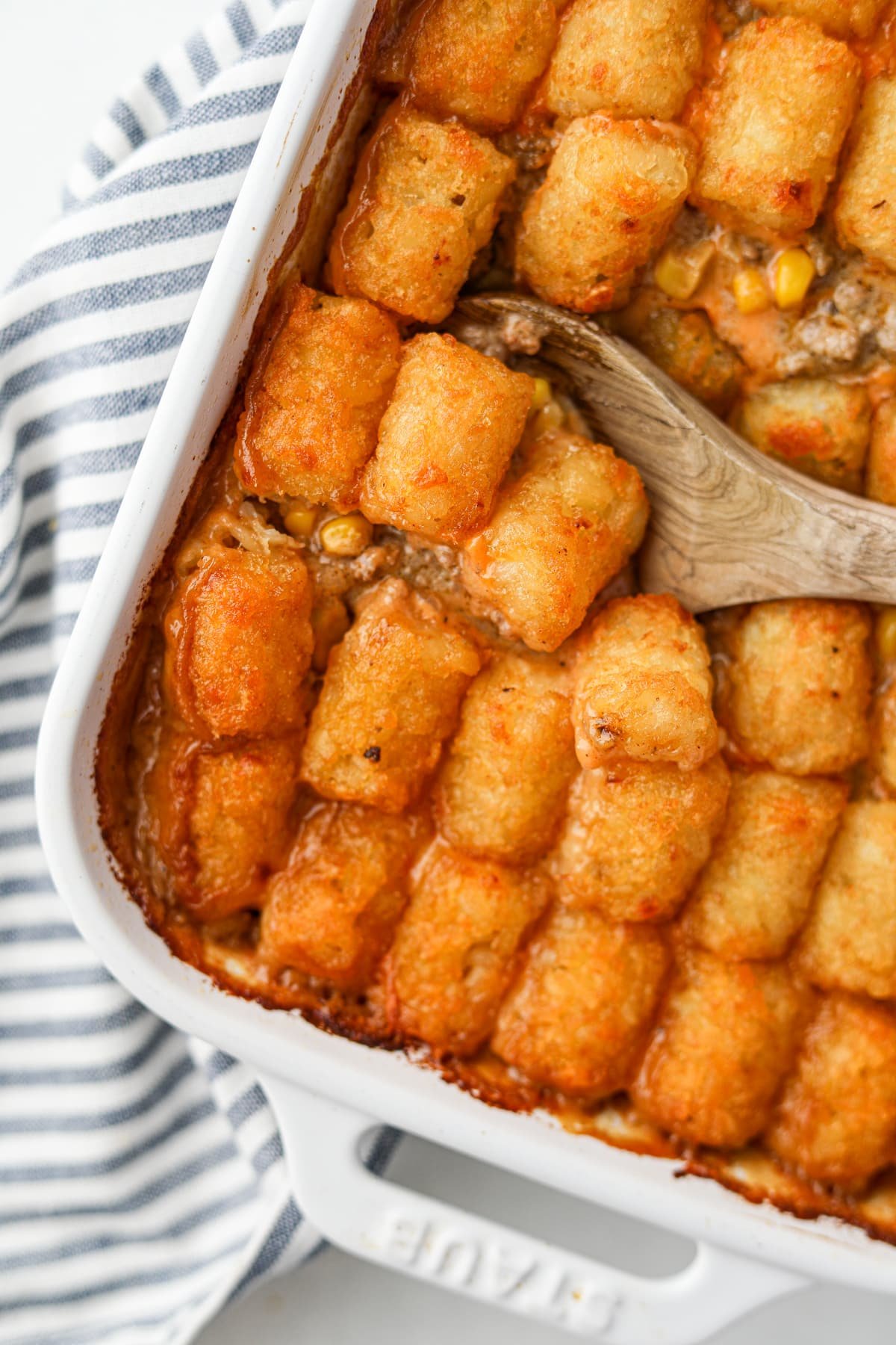 A wooden spoon scooping into a baking dish filled with Tater Tot Casserole.