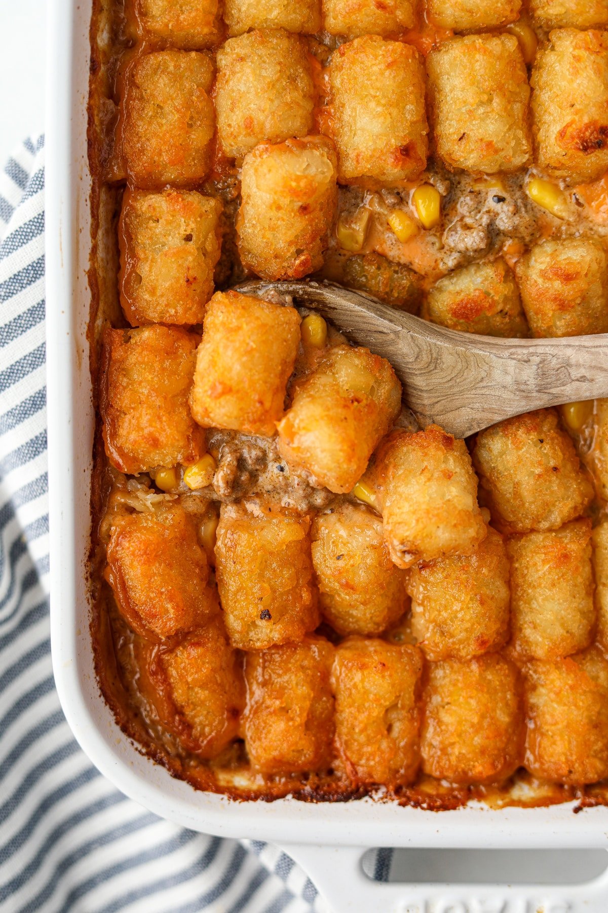 Dishing out a casserole that is topped with crispy potato tots.